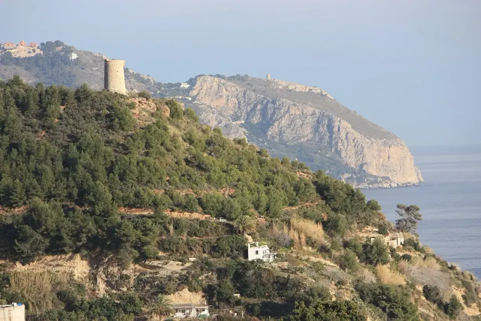 Torre de Maro sobre una loma de pinos, con los acantilados de Cerro Gordo al fondo