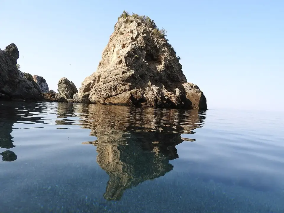 Roca que sale del agua en calma en la cala del Cañuelo, en Maro