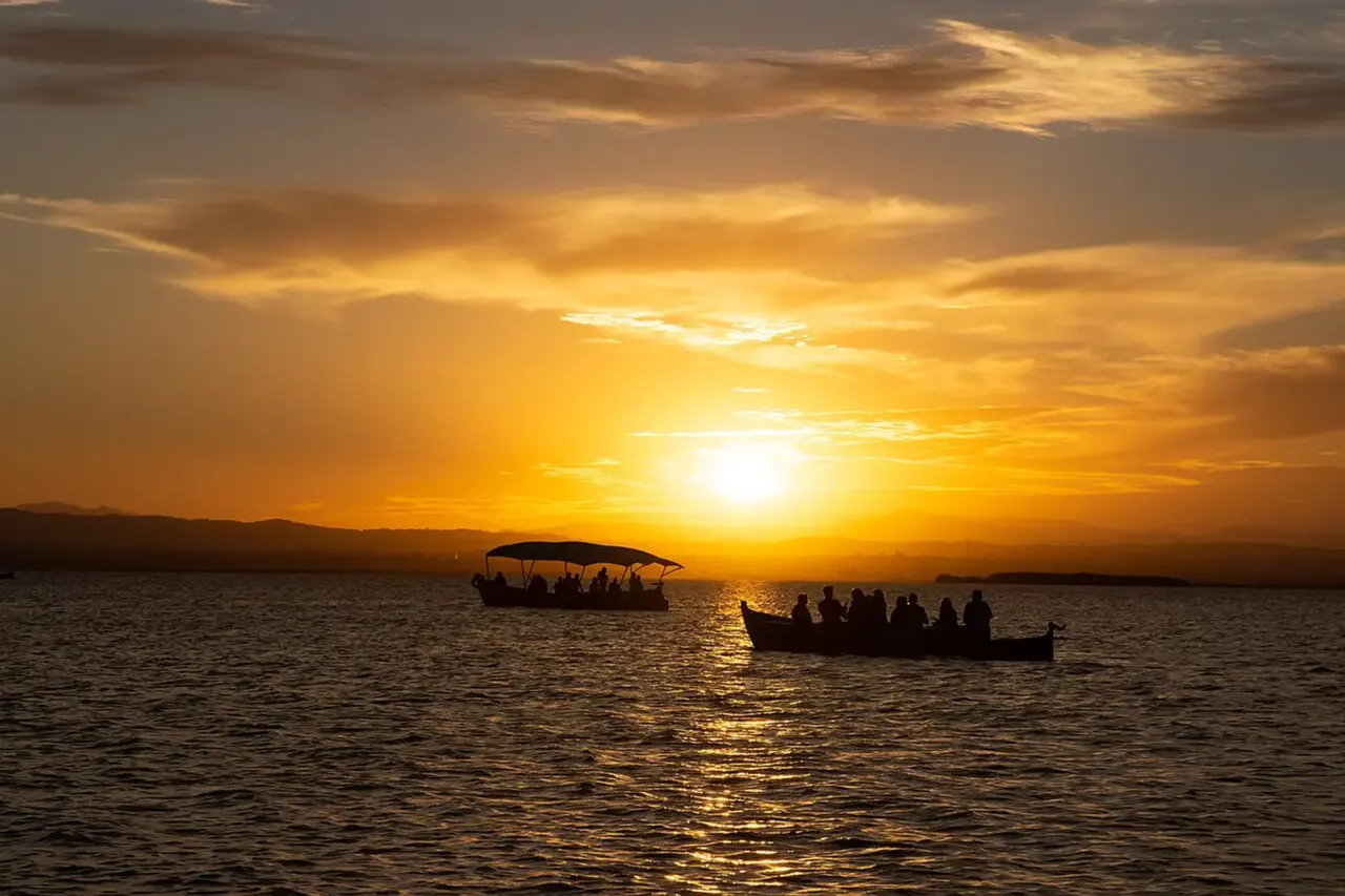 Puesta de sol sobre el lago de la Albufera con dos barcas llenas de visitantes a contraluz y las montañas al fondo