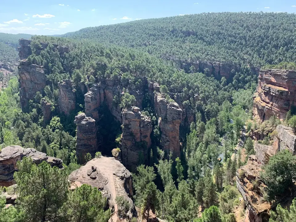 Torreones de arenisca roja entre pinos en el barranco de la Hoz, con laderas boscosas al fondo