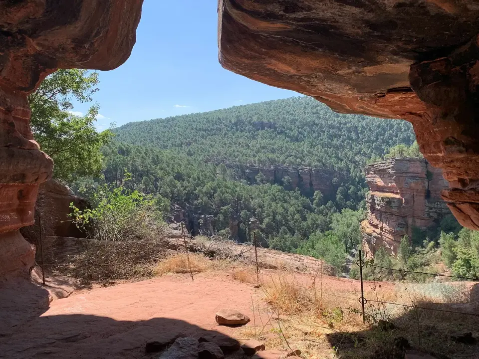 Vista del barranco de la Hoz enmarcada por un abrigo de roca roja, con pinares y paredes de arenisca al fondo