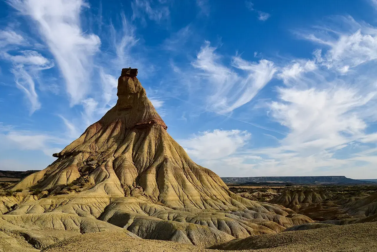 Castildetierra, chimenea de arcilla y arenisca con un sombrero de roca en la cima, bajo un cielo azul con nubes en la Bardena Blanca