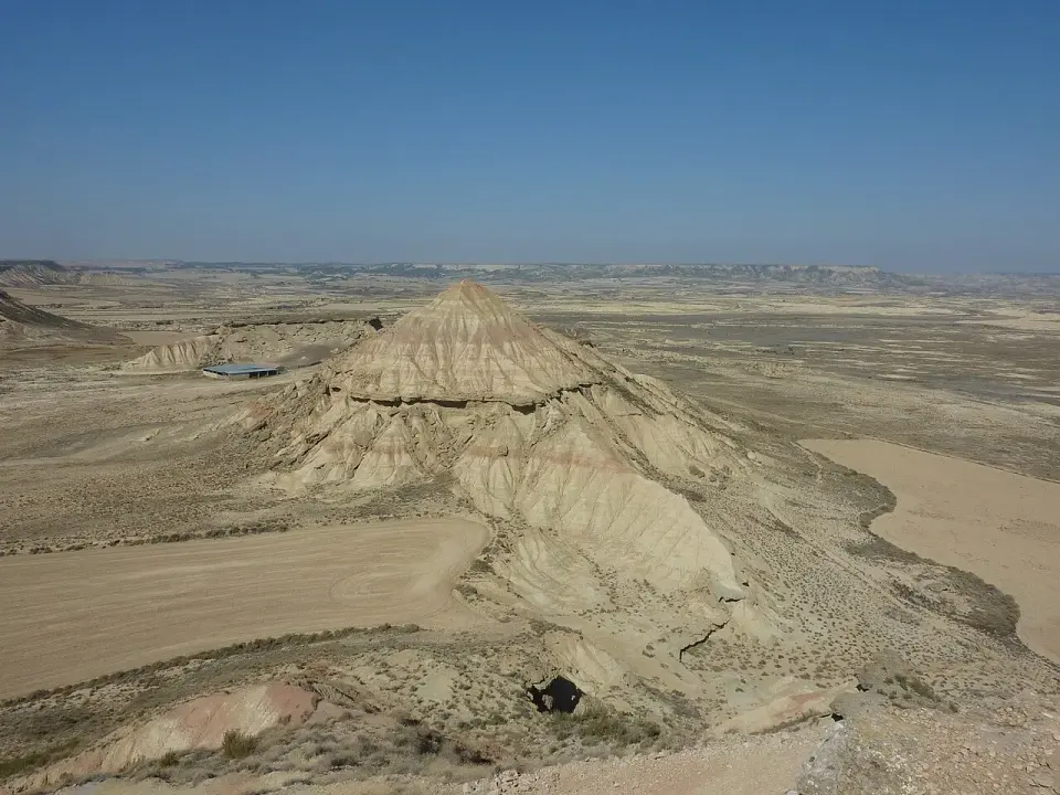 Cabezo de laderas erosionadas en medio de la llanura árida de la Bardena Blanca, con pistas de tierra y mesetas al fondo