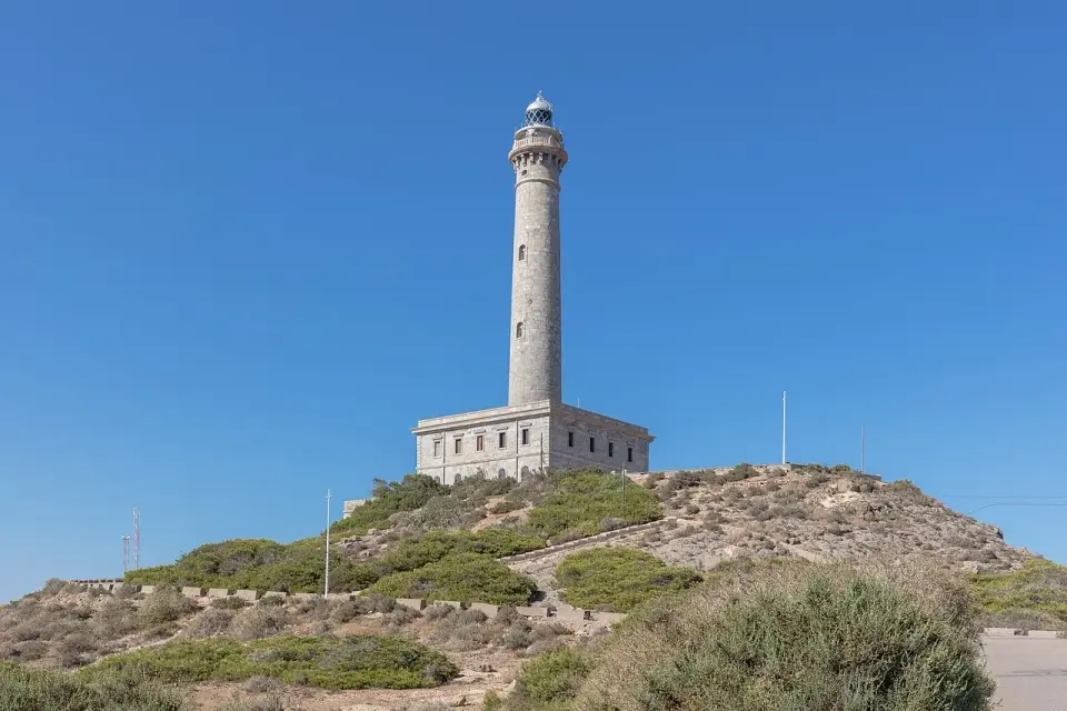 Faro de Cabo de Palos, torre blanca de piedra sobre un promontorio con matorral bajo un cielo azul