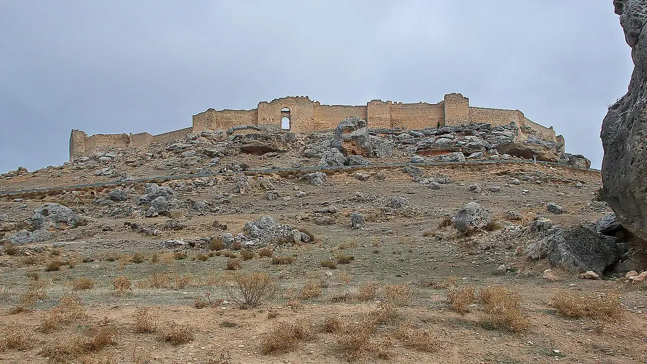 Murallas del castillo califal de Gormaz extendidas sobre un cerro pedregoso de matorral bajo un cielo nublado