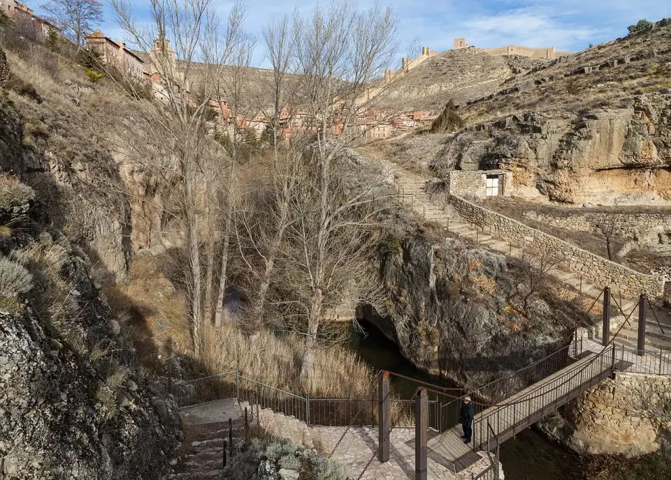 Pasarela junto al río Guadalaviar en Albarracín, entre paredes de roca, con las murallas en lo alto del cerro
