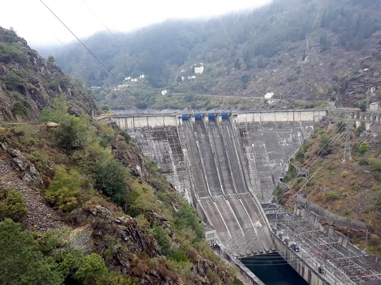 Presa de Salime sobre el río Navia, con su muro de hormigón y sus aliviaderos entre laderas de monte y casas en lo alto