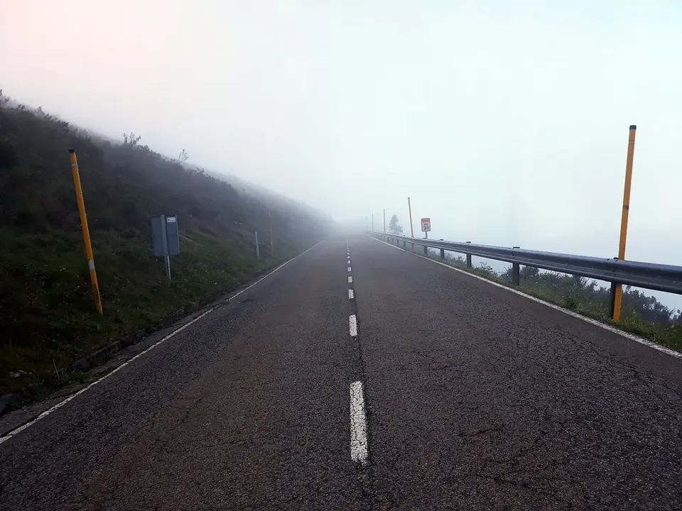 Carretera de montaña en el puerto del Palo envuelta en niebla, con quitamiedos y balizas amarillas a ambos lados