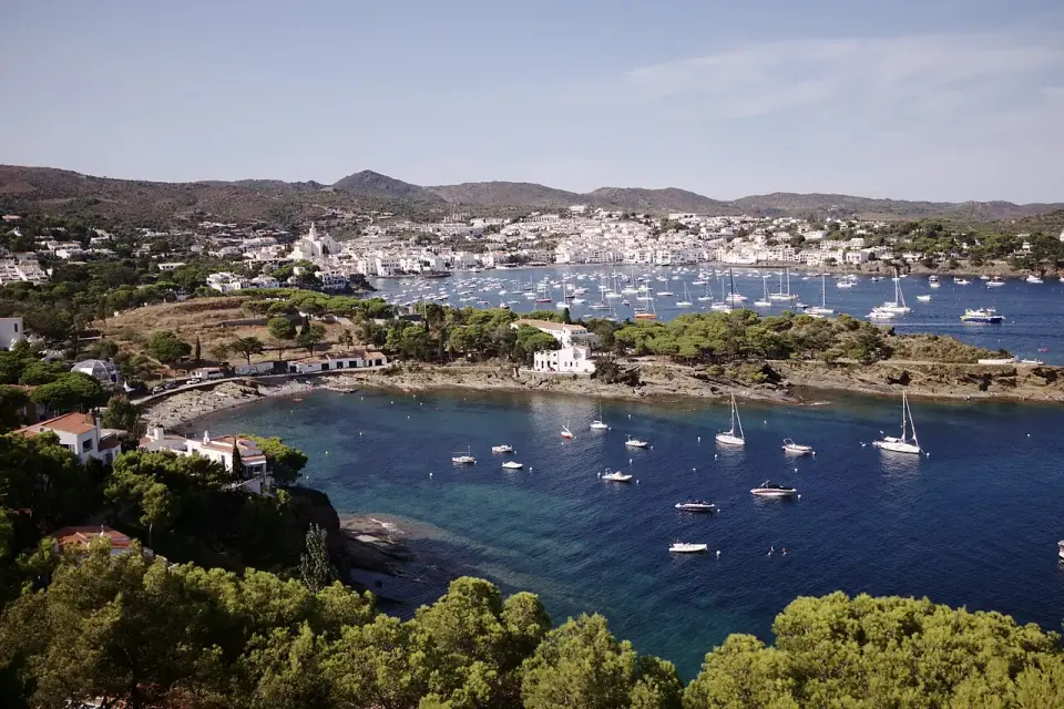 Bahía de Cadaqués con veleros fondeados y el pueblo blanco al fondo, entre colinas