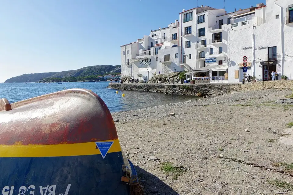 Casas blancas del frente marítimo de Cadaqués junto a la playa, con una barca en primer plano