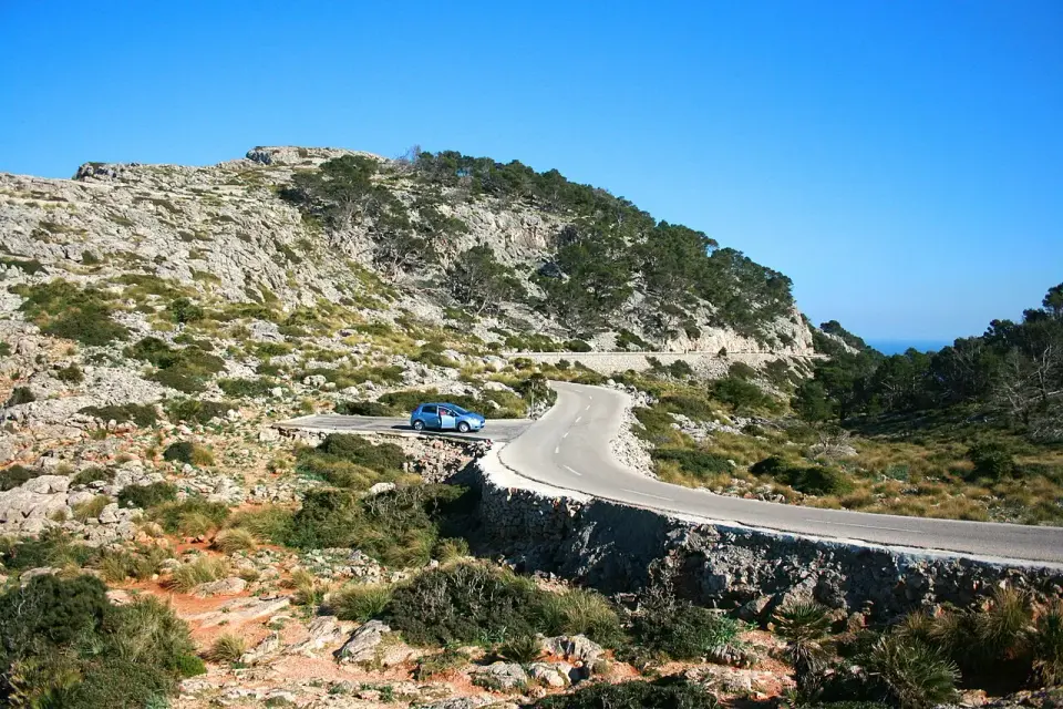 Curva de la MA-2210 con un muro de piedra entre colinas de pinar y matorral en la península de Formentor
