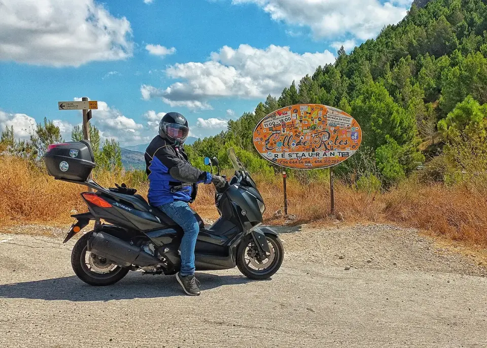 Motorista con su moto junto al cartel del Coll de Rates, en lo alto del puerto