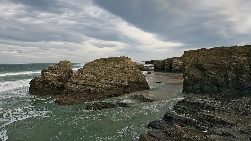 Rocas y acantilados de la playa de As Catedrais, en Ribadeo, con el mar entrando entre ellos bajo un cielo nublado