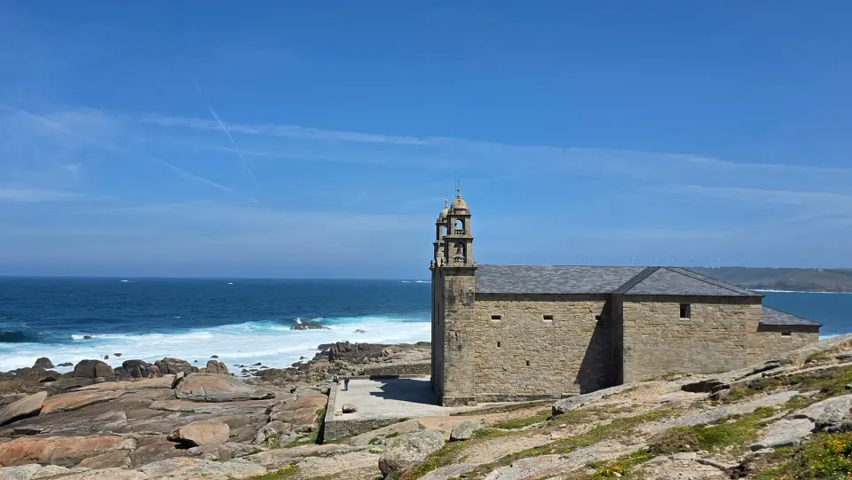 Santuario de piedra da Virxe da Barca sobre las rocas de la costa de Muxía, con olas rompiendo al fondo