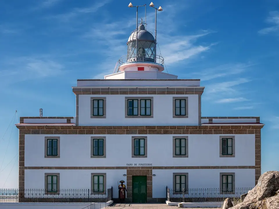 Edificio de piedra y cristal del faro de Fisterra bajo un cielo azul