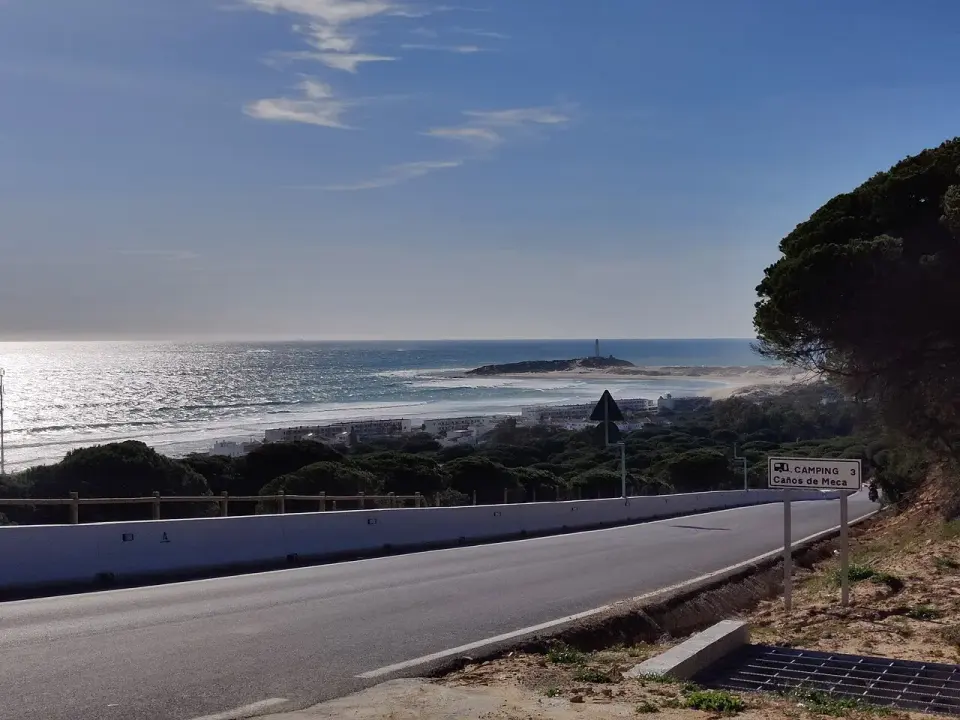 Carretera junto a la costa de Los Caños de Meca, con el cabo de Trafalgar y su faro al fondo sobre el mar