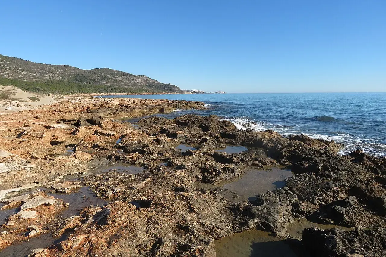 Costa rocosa de la Serra d'Irta con charcas entre las rocas, el mar azul y la sierra al fondo