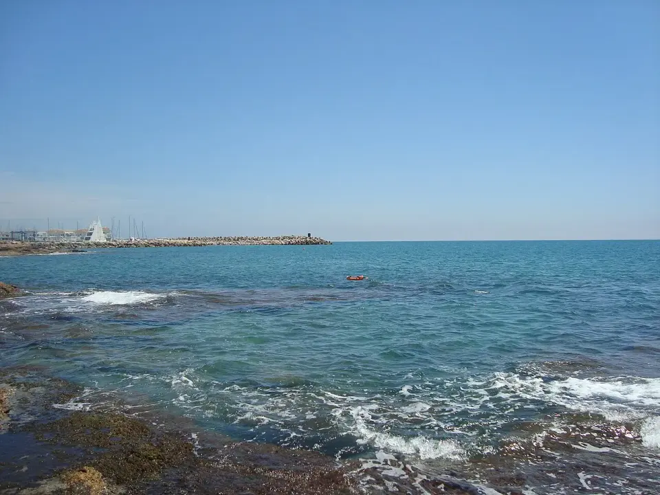 Mar Mediterráneo con oleaje sobre las rocas en Alcossebre y el puerto deportivo al fondo