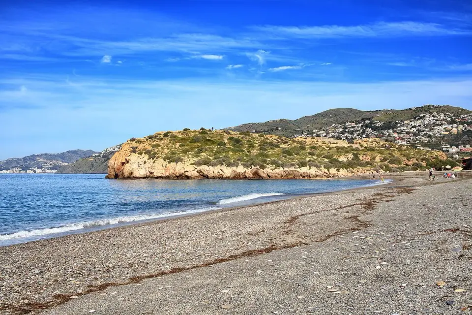 Playa de grava junto al peñón de Salobreña, con el agua clara y las casas en la ladera