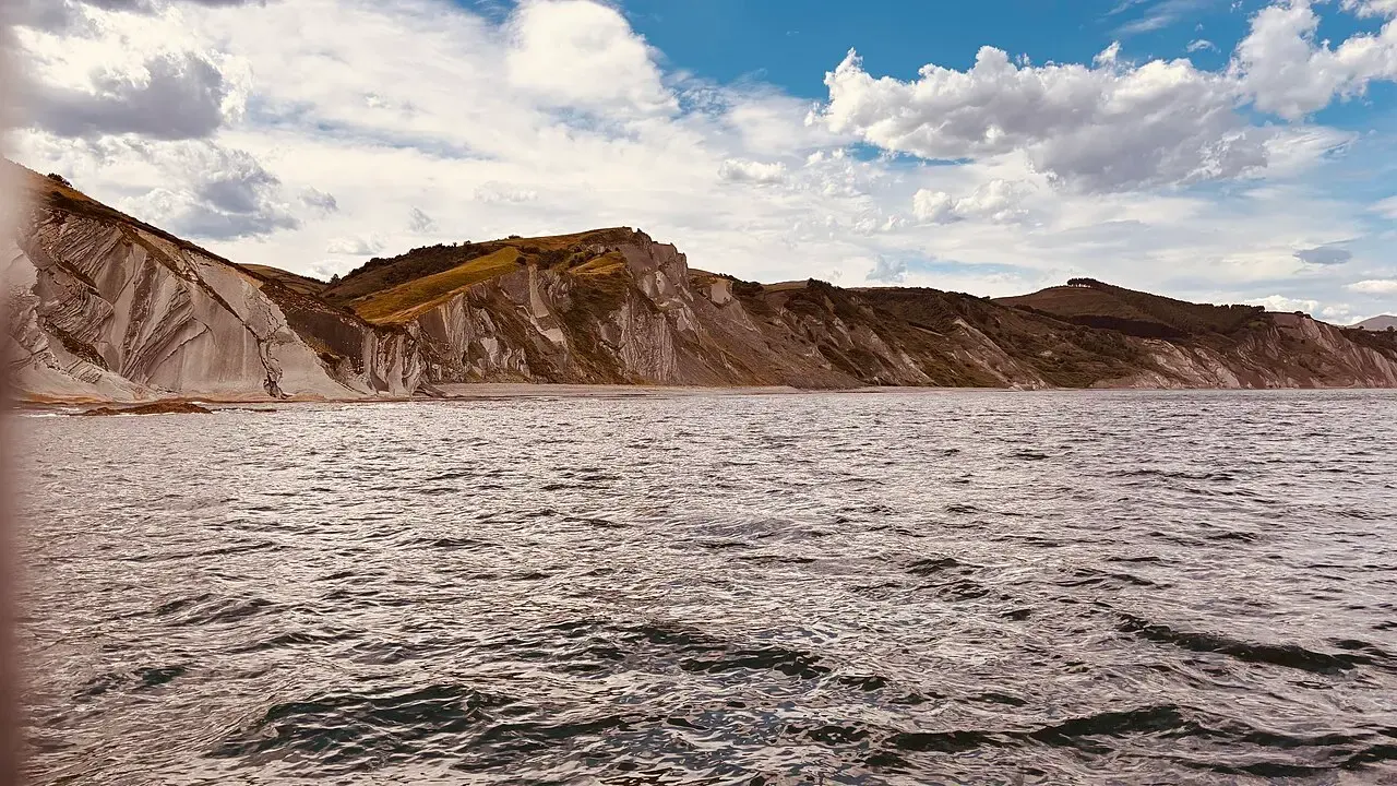 Acantilados de flysch con estratos inclinados en la costa de Zumaia, vistos desde el mar bajo un cielo con nubes