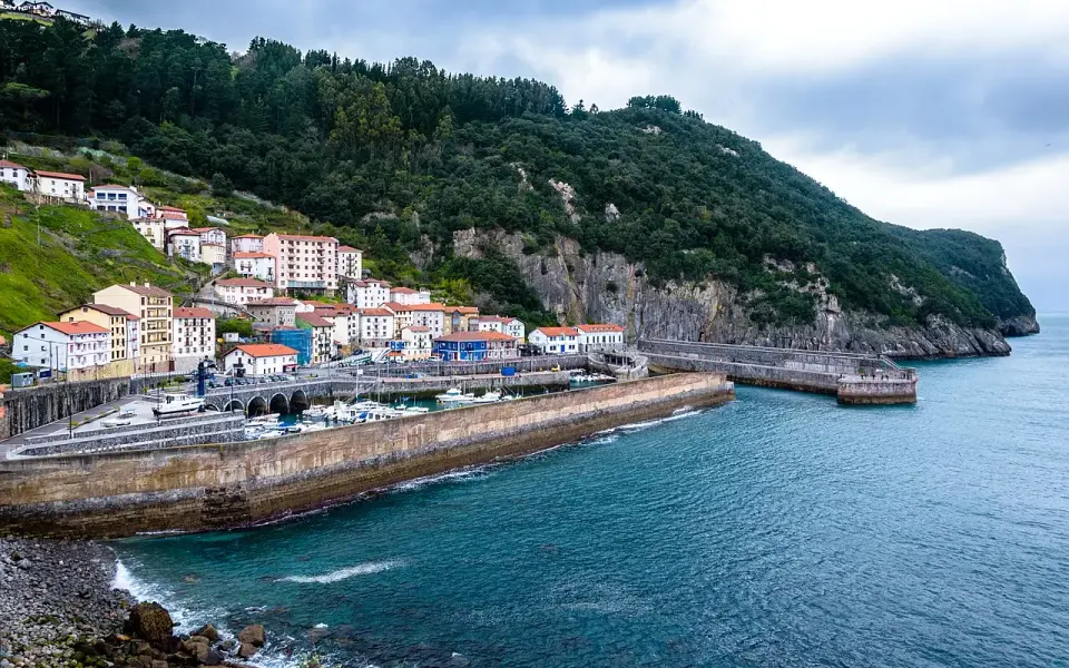 Casas de Elantxobe escalonadas sobre la ladera del cabo Ogoño, con el puerto pesquero y su espigón en primer plano