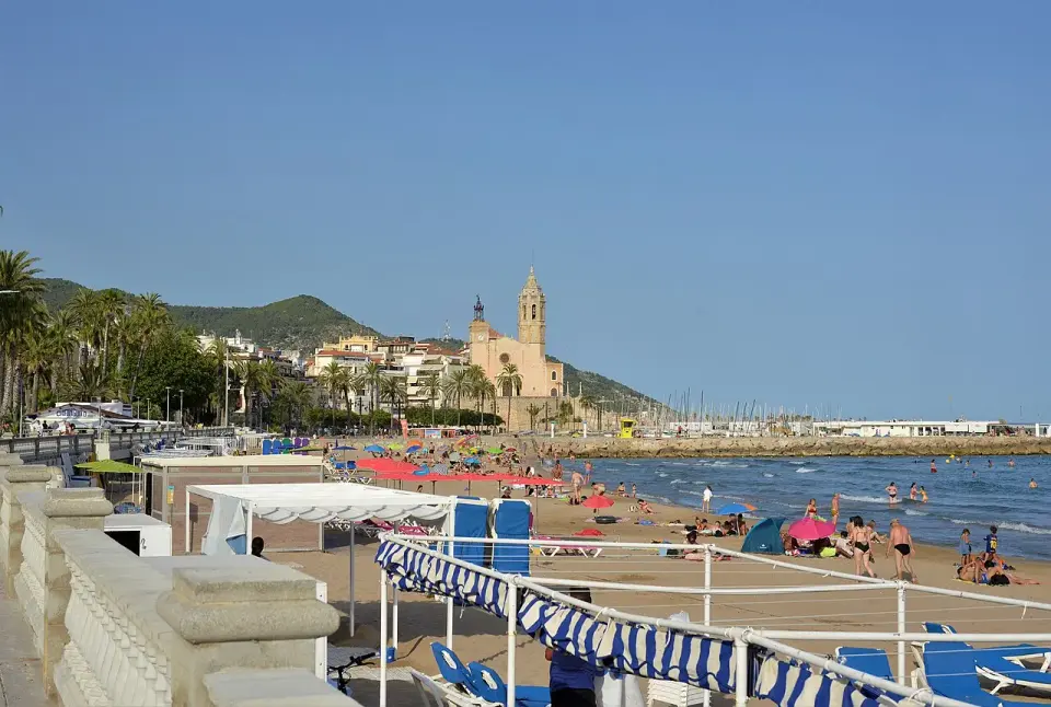 Paseo marítimo de Sitges junto a la playa, con la iglesia de Sant Bartomeu i Santa Tecla al fondo