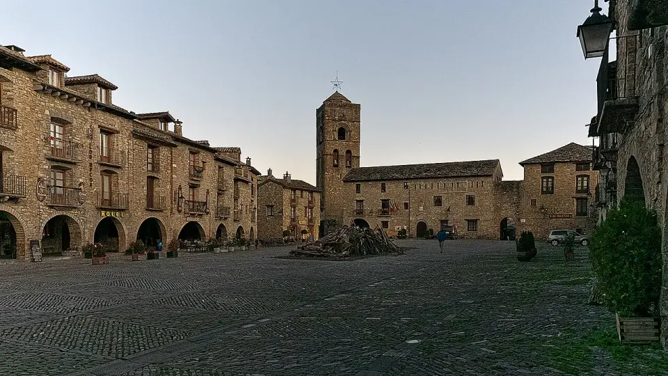 Plaza Mayor porticada de Aínsa con casas de piedra y la torre de la iglesia de Santa María al fondo