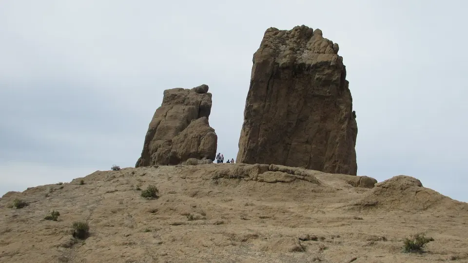 El Roque Nublo y el Roque del Fraile sobre la plataforma rocosa, con varias personas al pie del monolito que dan idea de su tamaño