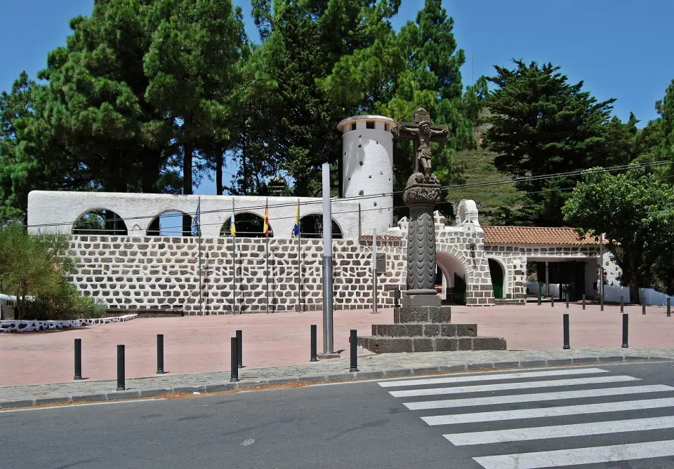La cruz de piedra de la Cruz de Tejeda sobre su pedestal, junto al muro encalado del parador y los pinos de la cumbre