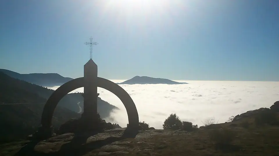 Monumento con una cruz en el puerto del Pico a contraluz, sobre un mar de nubes que cubre el valle