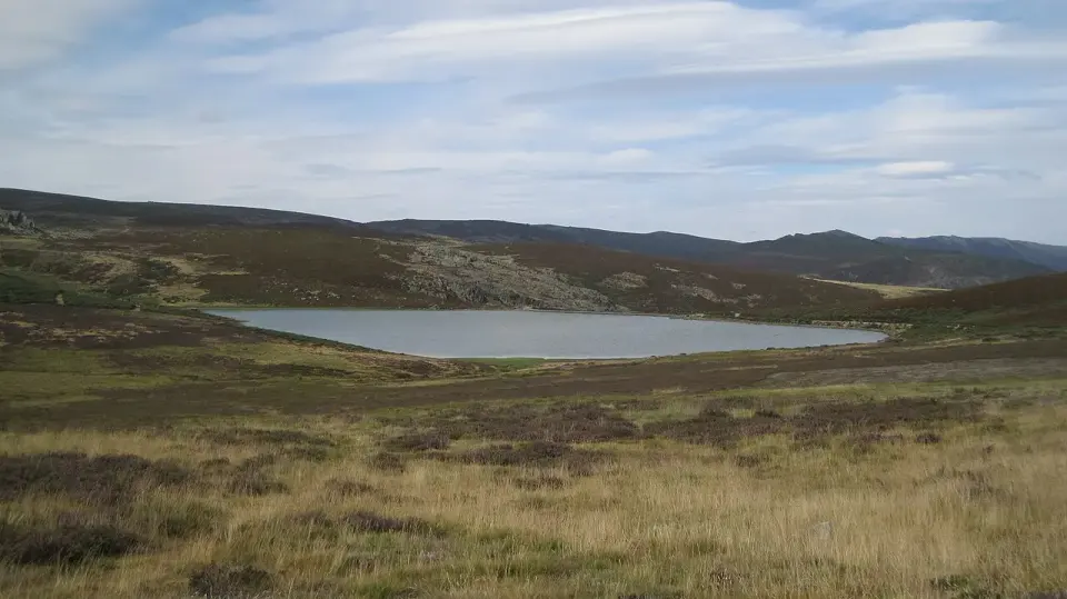 Laguna de los Peces en una meseta de brezos y pastos de alta montaña, bajo un cielo con nubes
