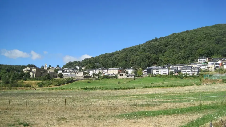 San Martín de Castañeda en una ladera verde, con el monasterio a la izquierda y casas de pizarra bajo un monte de robles