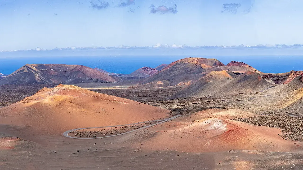 Volcanes rojizos y ocres del parque nacional de Timanfaya con una carretera que serpentea y el mar al fondo