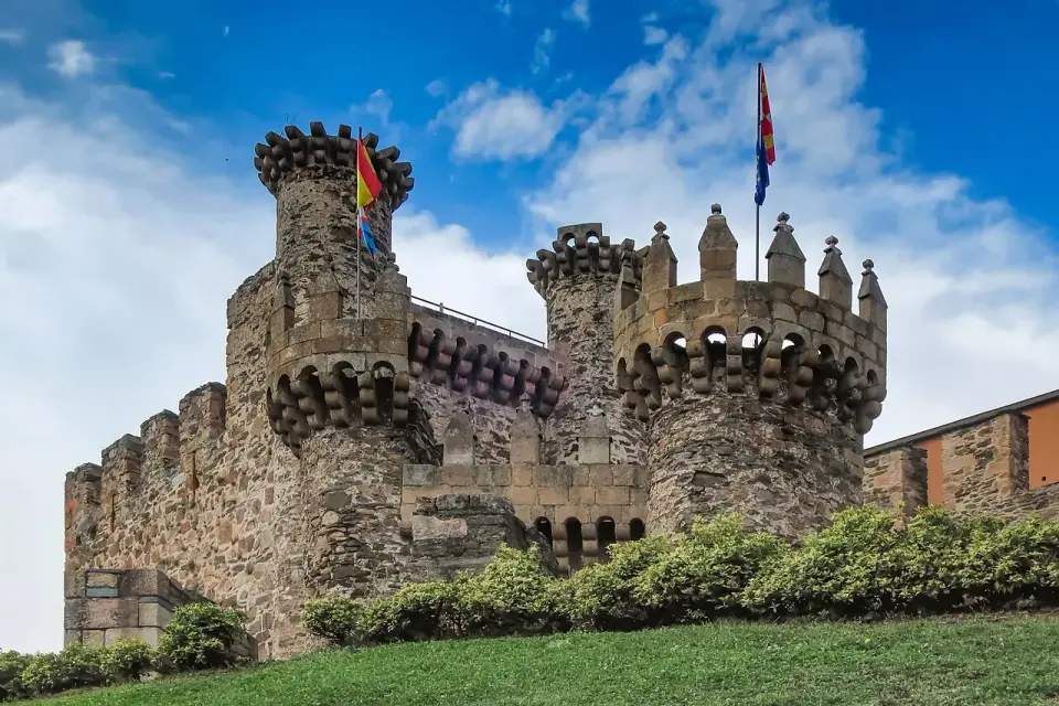 Torres almenadas del castillo de los Templarios de Ponferrada con banderas, bajo un cielo azul con nubes