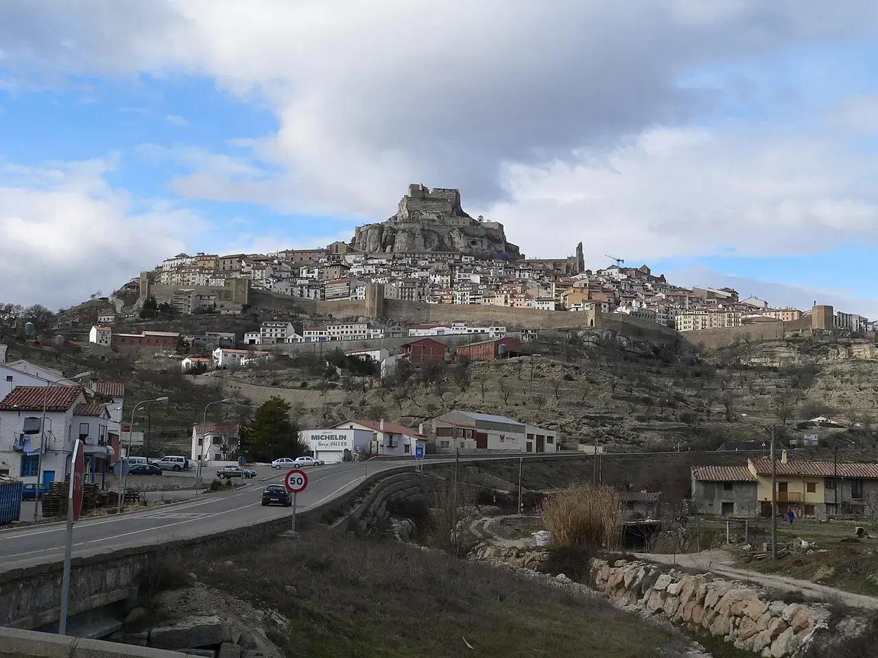 Morella sobre su cerro, con el castillo en lo alto y las murallas rodeando el pueblo, vista desde la carretera de acceso