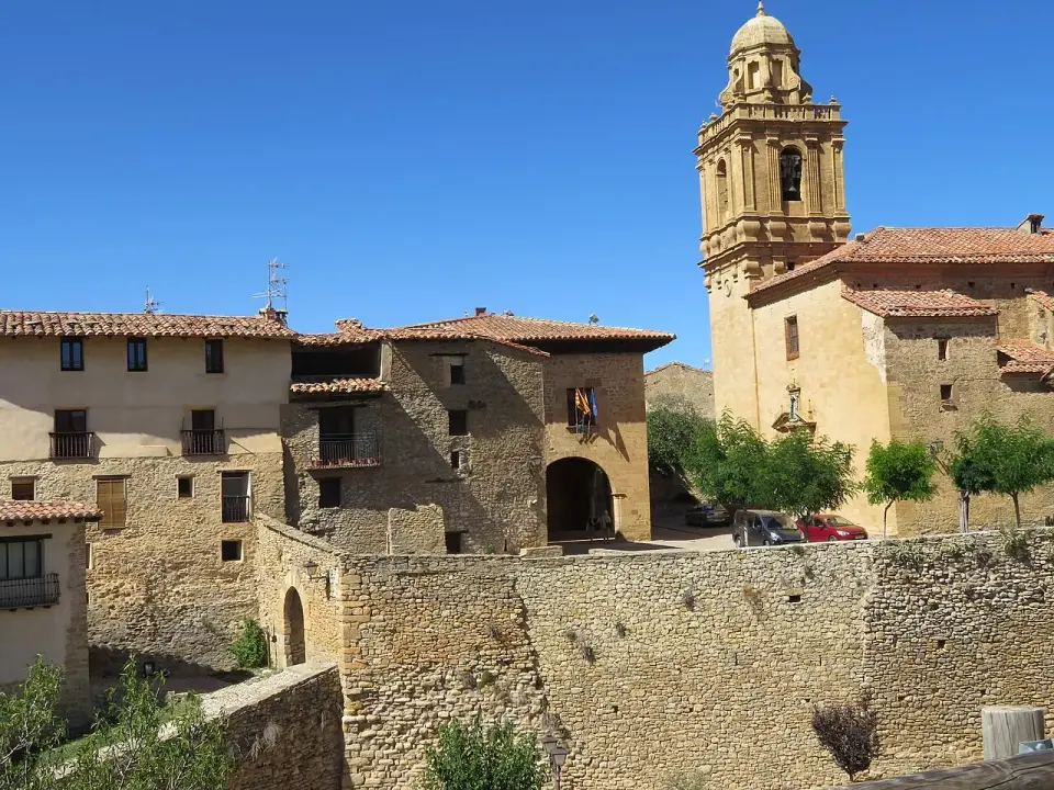 Casas de piedra, muralla y torre barroca de la iglesia de Mirambel bajo un cielo azul