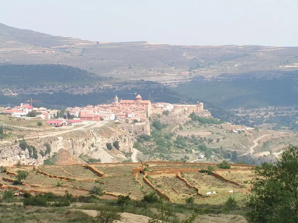 Cantavieja sobre un espolón rocoso, con la iglesia y las casas al borde del barranco y montañas al fondo