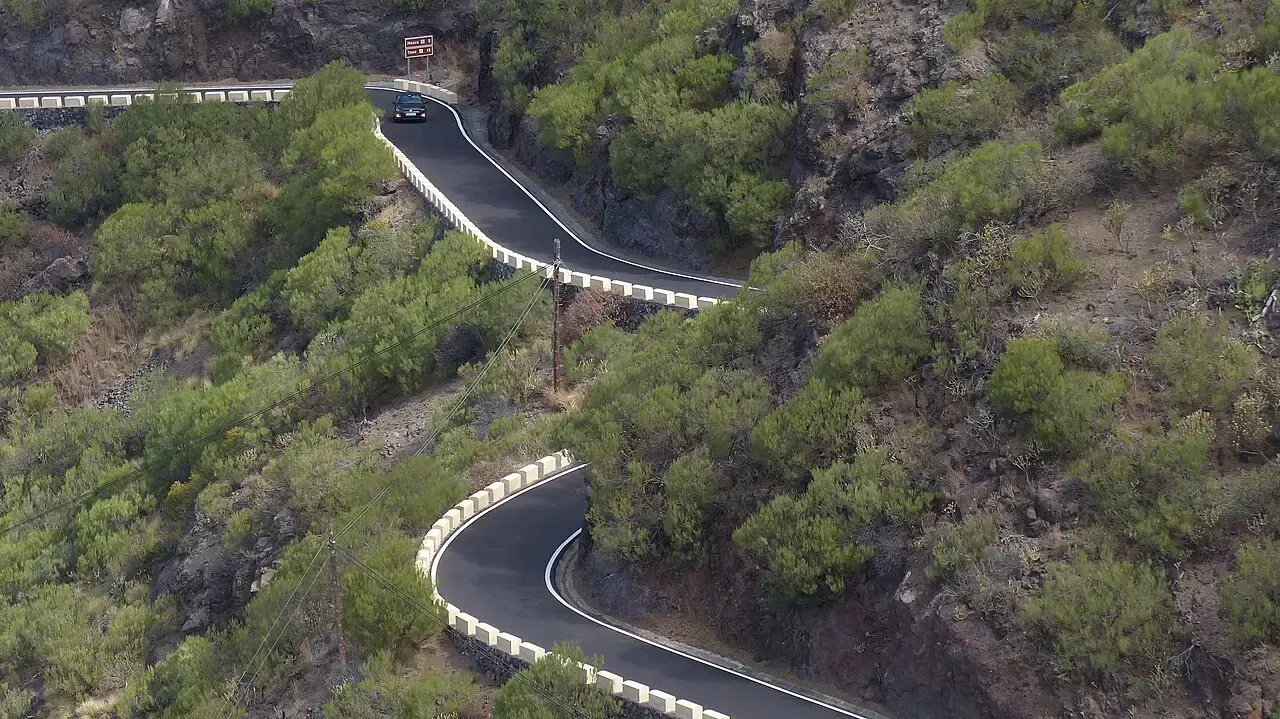 Carretera TF-436 serpenteando en horquillas por una ladera de vegetación verde en el valle de Masca