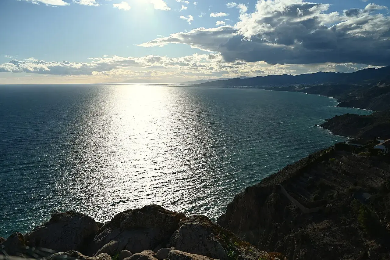 Acantilados de Maro-Cerro Gordo cayendo sobre el Mediterráneo, con la costa de la Axarquía al fondo y el sol reflejado en el mar