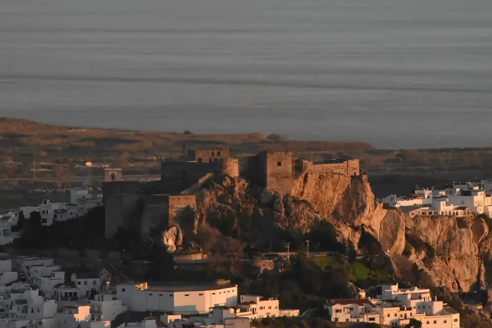 Castillo de Salobreña sobre un peñón, rodeado de casas blancas, con el mar detrás al atardecer