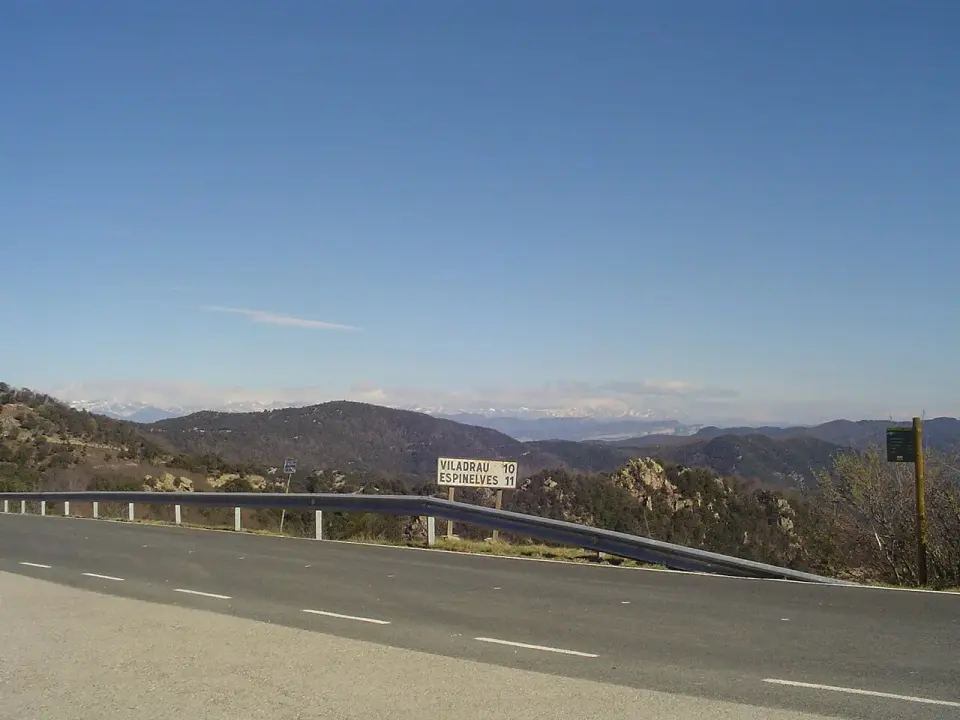 Carretera con guardarraíl y cartel en el coll de Sant Marçal, con montañas azuladas al fondo