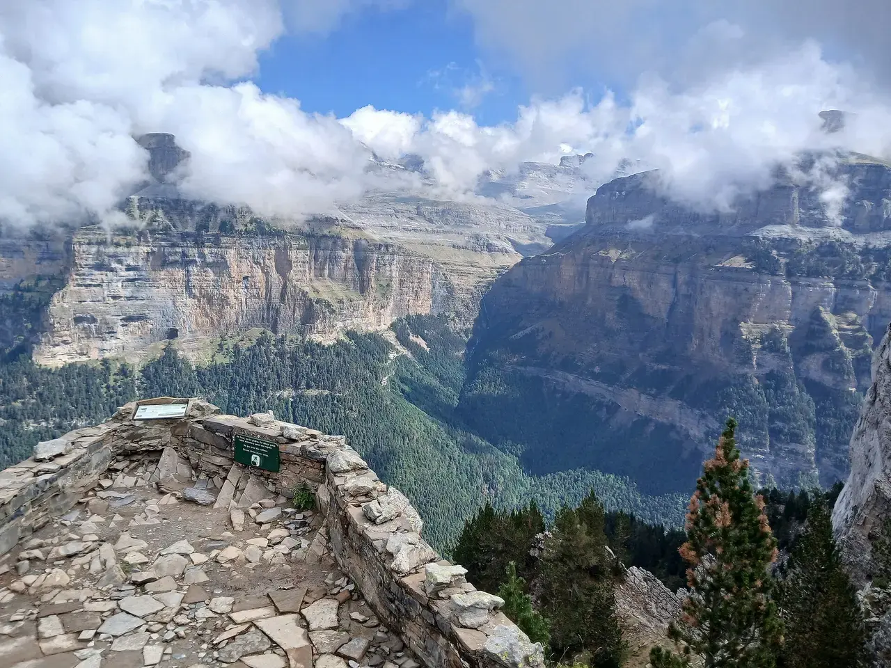 Valle de Ordesa visto desde un mirador de piedra, con grandes paredes de caliza y bosque en el fondo del valle bajo nubes