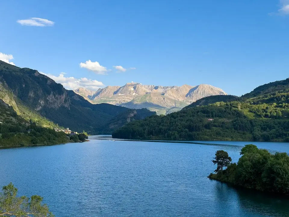 Embalse de Lanuza de aguas azules entre montañas boscosas, con picos del Pirineo al fondo