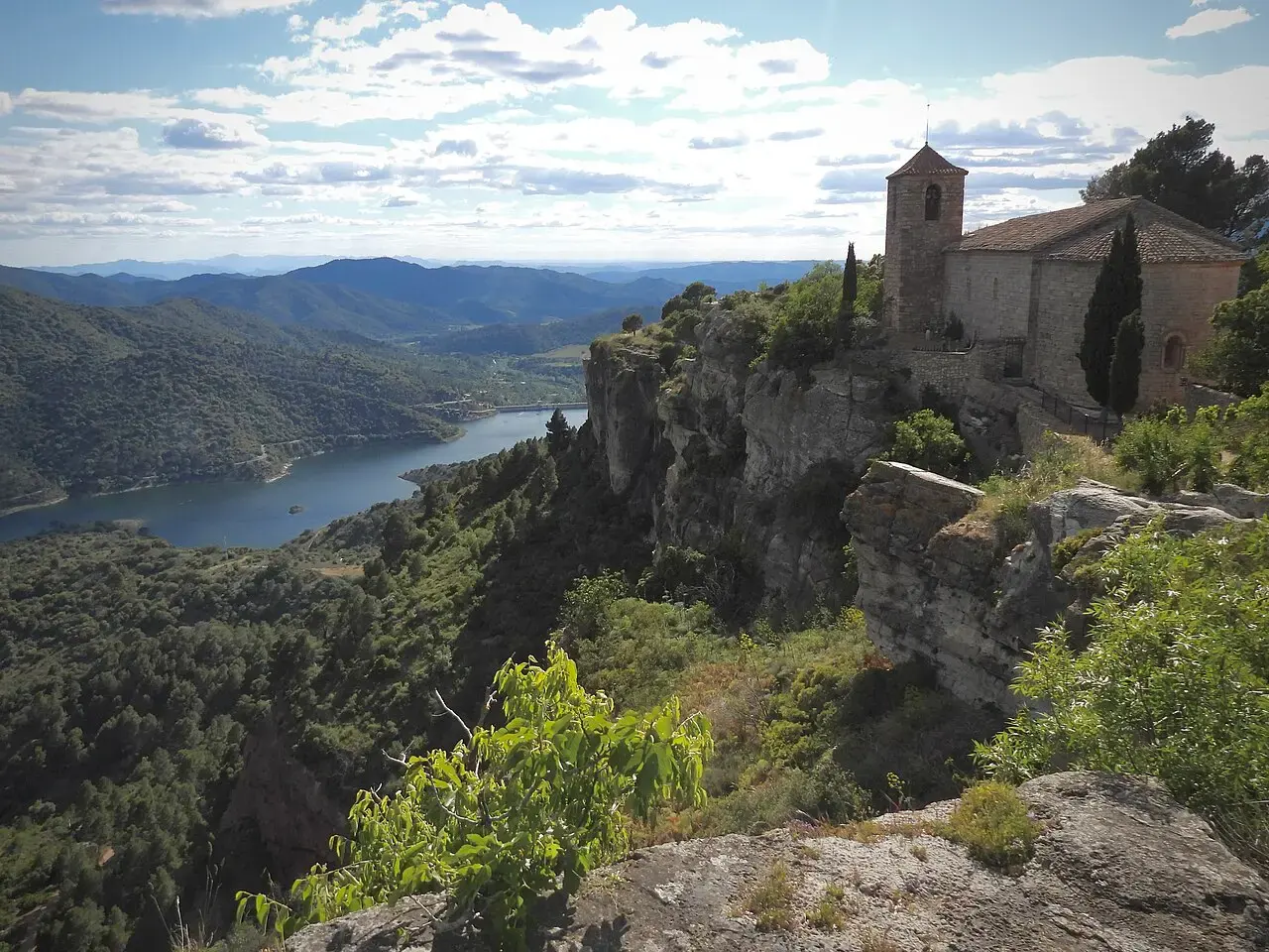 Iglesia románica de Santa María de Siurana al borde de un acantilado, con el embalse de Siurana y las sierras del Priorat al fondo