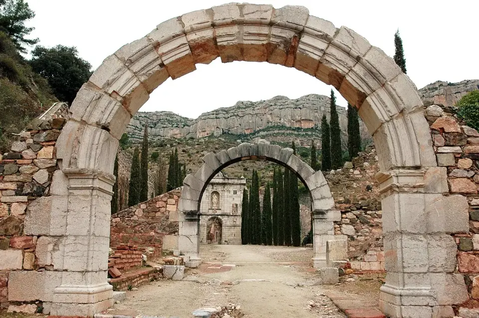 Arcos de piedra de la cartuja de Escaladei en ruinas, con una avenida de cipreses y las paredes del Montsant detrás