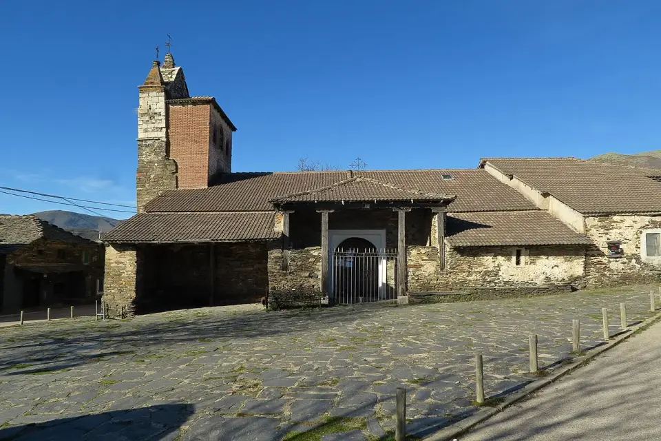 Iglesia de San Juan Bautista de Majaelrayo, de piedra oscura, con su torre y un pórtico de madera bajo cielo azul