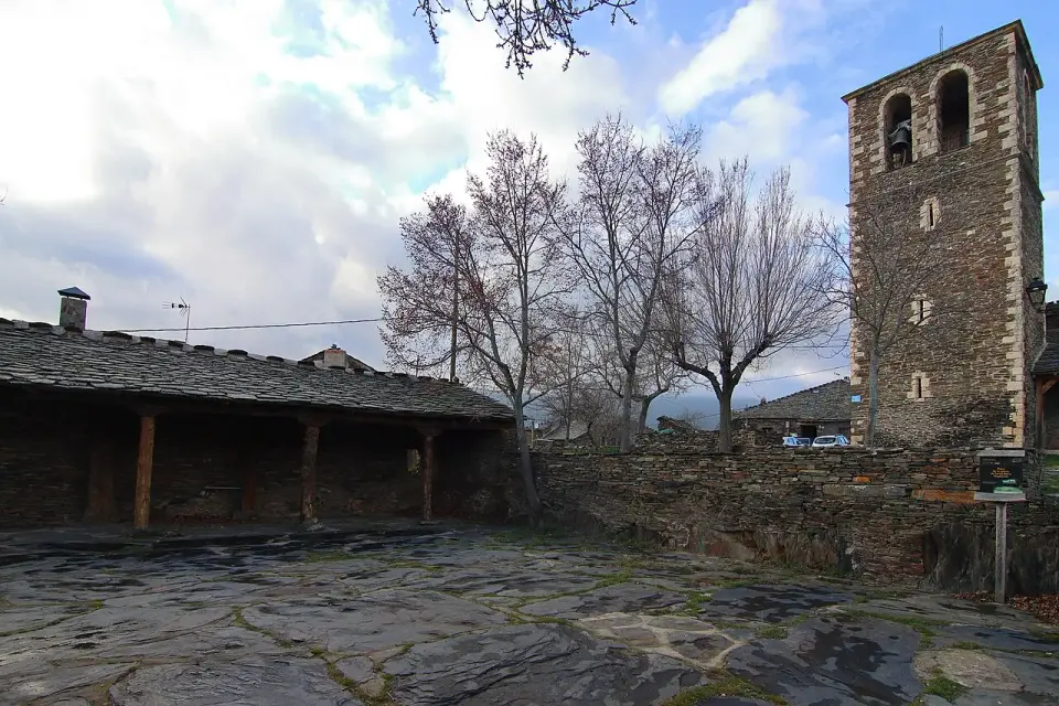 Plaza de la iglesia de Campillo de Ranas, empedrada con lajas de pizarra, con la torre y un pórtico de madera