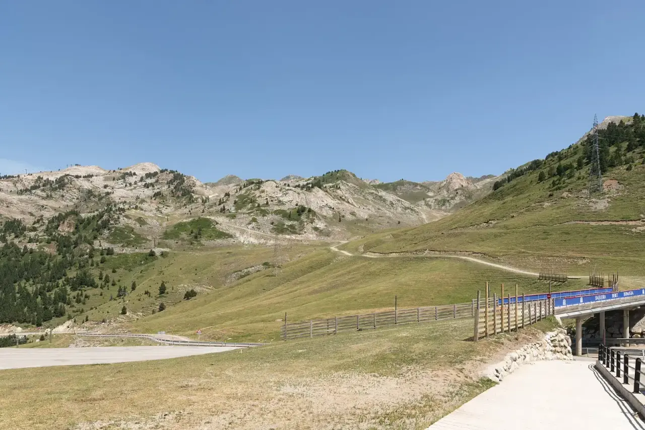 Explanada del Port de la Bonaigua en verano, con prados, pinos y la carretera C-28 en la cima del puerto