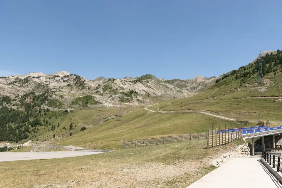 Explanada del Port de la Bonaigua en verano, con prados, pinos y la carretera C-28 en la cima del puerto