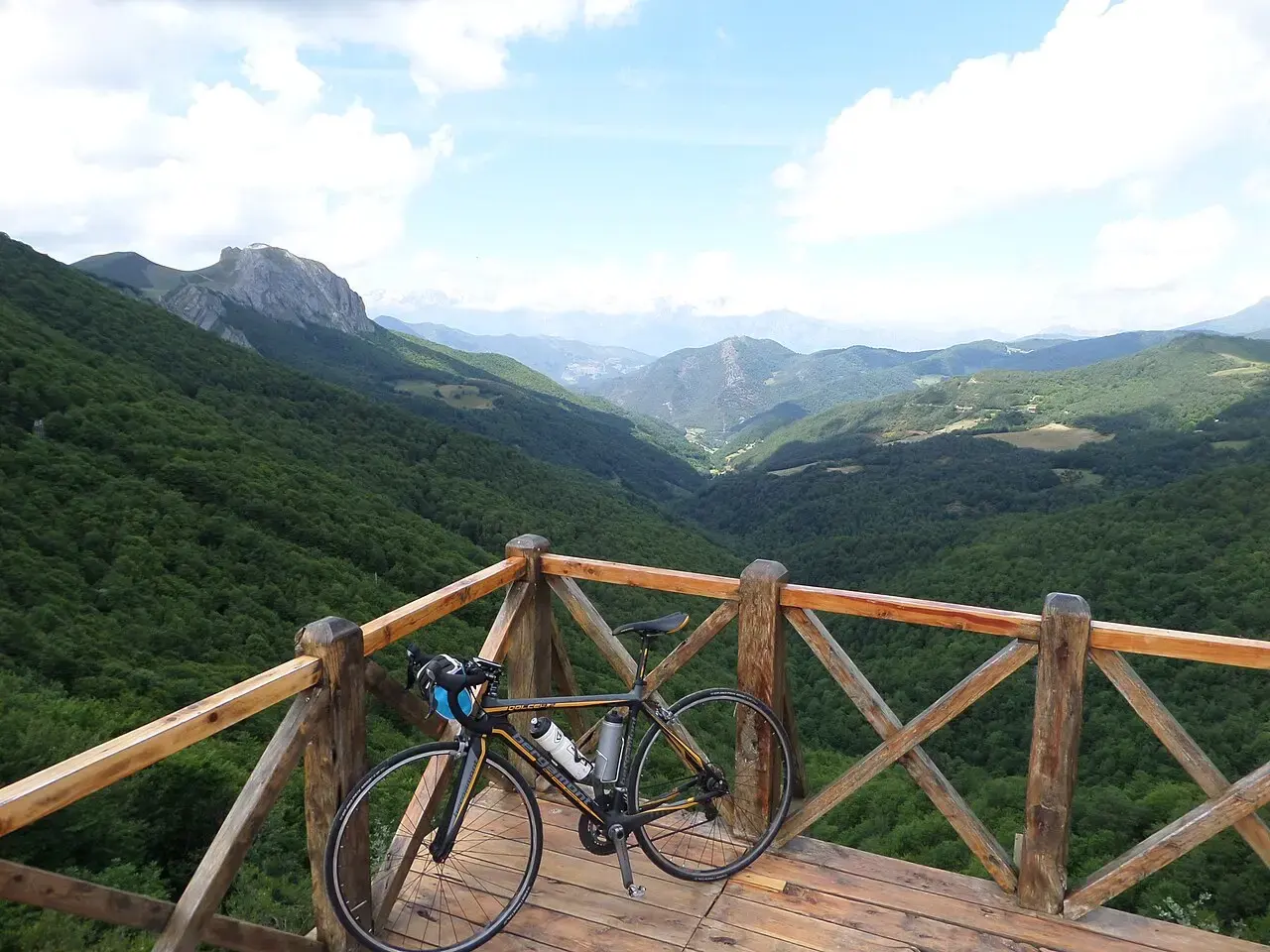 Mirador de madera en el puerto de Piedrasluengas, con una bicicleta apoyada en la barandilla y vistas a los valles verdes y las montañas de Liébana